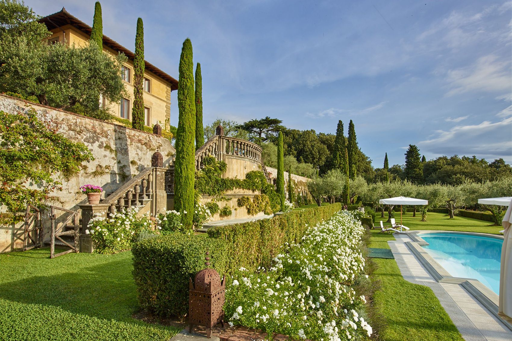 The outdoor pool and garden of Il Palagio in Tuscany. Stairs by a wall on the left lead up to the yellow villa.